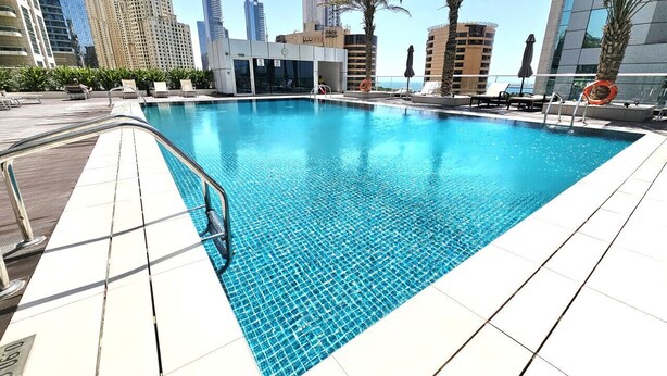 A swimming pool with a tiled deck, surrounded by palm trees and modern buildings.