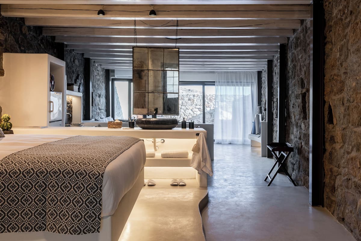A modern bedroom with a large bed, a built-in bathtub, and a stone wall.