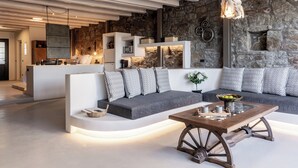 A modern living room with a stone wall, a wooden coffee table, and a sofa with patterned cushions. - Makani Suites (Mykonos)