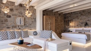 A modern living room with a stone wall, white sofas, a wooden coffee table, and a fireplace. - Makani Suites (Mykonos)