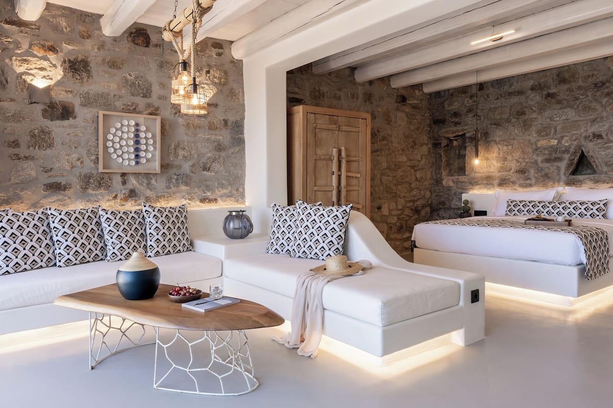A modern living room with a stone wall, white sofas, a wooden coffee table, and a fireplace.
