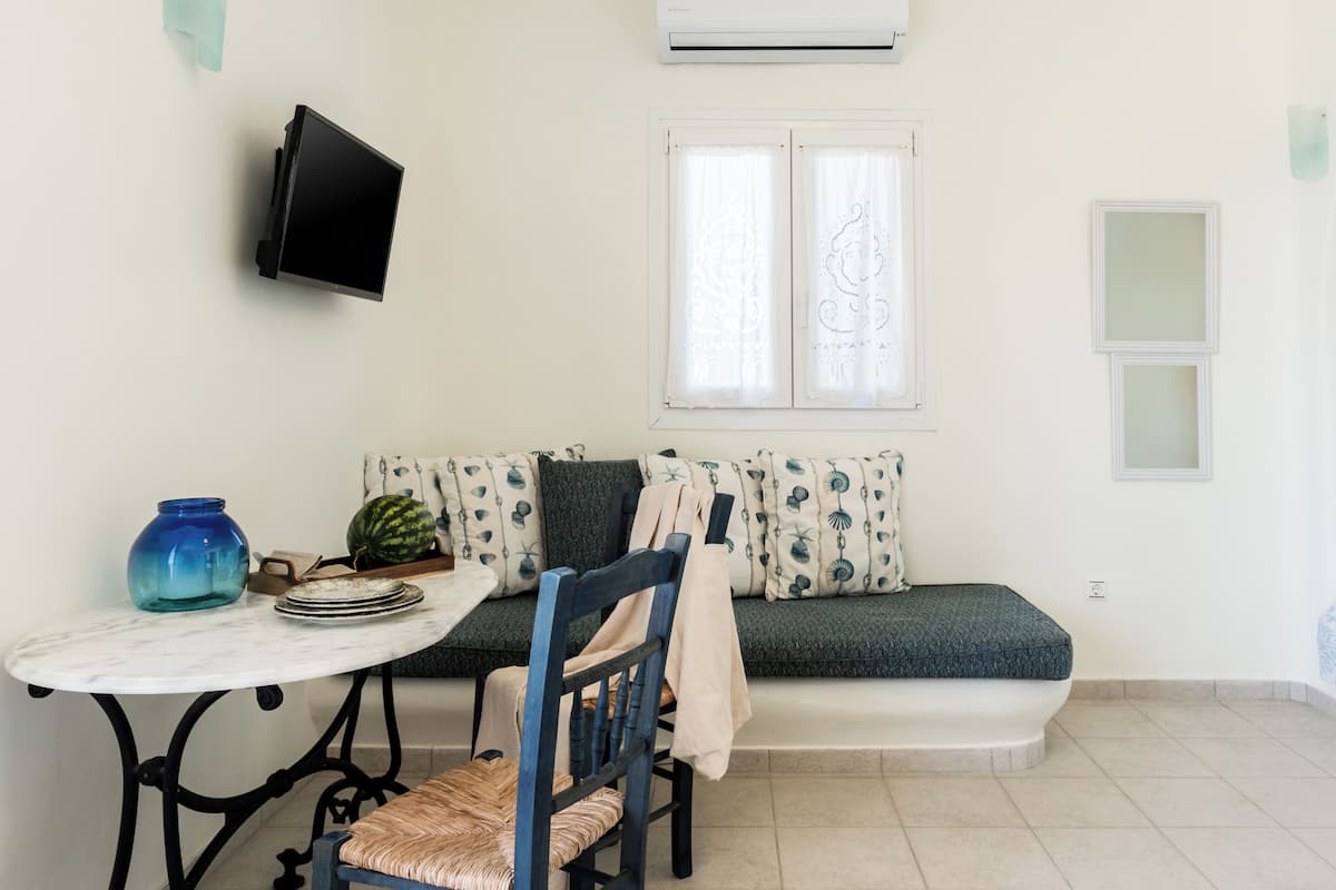 A room with a round table, a blue chair, a sofa with patterned cushions, and a wall-mounted TV.