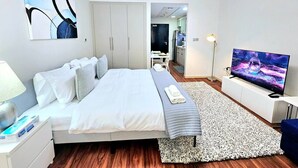 Una camera da letto moderna con un letto grande, una TV, una scrivania e un angolo cottura sullo sfondo.