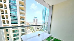 Un balcone con un tavolo e sedie in vetro, vista su edifici alti e pavimento verde artificiale.
