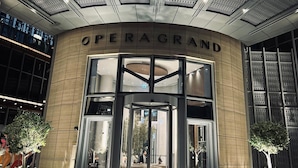 Indgangen til Opera Grand hotel med et moderne design, kendetegnet ved en markant indgang med glasdøre og et loft med geometrisk mønster.
