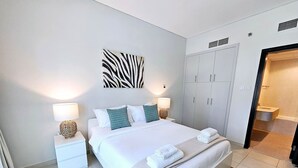 Une chambre d’hôtel moderne avec un grand lit, deux tables de chevet avec des lampes, une œuvre d’art à motifs zébrés accrochée au mur et une armoire.
