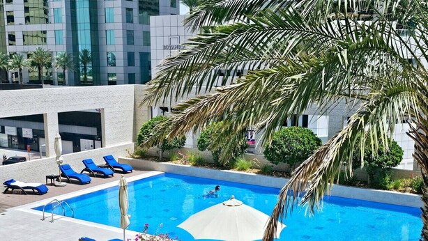 Une piscine entourée de palmiers et de verdure, avec des chaises longues et des parasols.