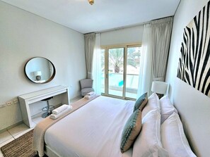 Hotellihuone, jossa on suuri sänky, pyöreä peili, yöpöytä, tuoli ja näkymä ulos.