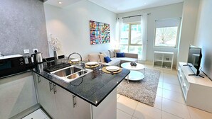 Une cuisine moderne dotée d’un îlot central, un coin repas avec une table ronde et un salon avec un canapé et un téléviseur.
