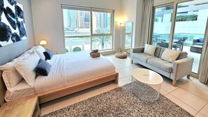 Une chambre d’hôtel moderne avec un grand lit, un canapé et une petite table basse. De grandes fenêtres offrent une vue sur la ville.