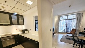 A modern kitchen with black cabinets and a built-in oven, leading to a dining area with a table and chairs. - Sunrise Homes - A Lovely 1-BR Apartment near JBR Marina (Dubai Marina)
