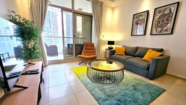 A modern living room with a sofa, armchair, coffee table, and a desk with a computer. - Sunrise Homes - A Lovely 1-BR Apartment near JBR Marina (Dubai Marina)