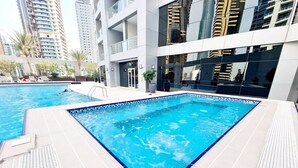 A rectangular swimming pool with a blue border, surrounded by a white tiled deck. - Sunrise Homes - A Lovely 1-BR Apartment near JBR Marina (Dubai Marina)