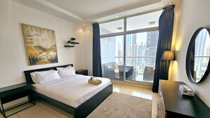A modern hotel room with a large bed, a view of the city, and a balcony with a chair. - Sunrise Homes - A Lovely 1-BR Apartment near JBR Marina (Dubai Marina)