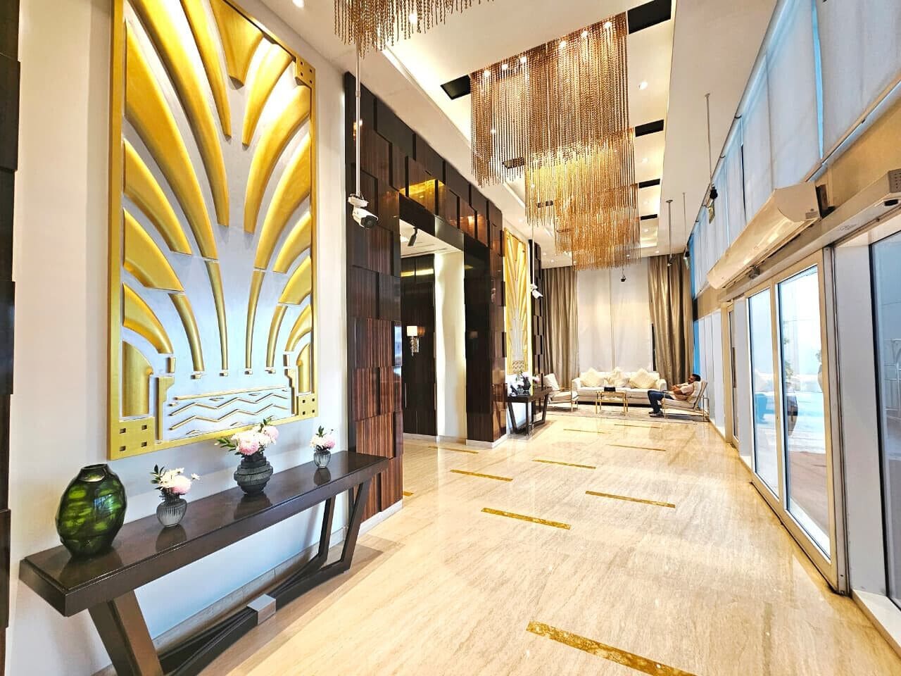 A modern hotel lobby with a long reception desk, a seating area with a sofa and chairs, and large windows offering a view.