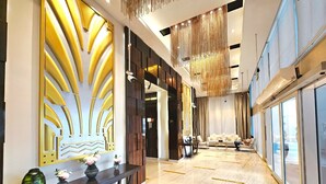 A modern hotel lobby with a long reception desk, a seating area with a sofa and chairs, and large windows offering a view.