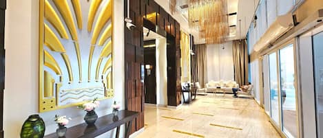 A modern hotel lobby with a long reception desk, a seating area with a sofa and chairs, and large windows offering a view.