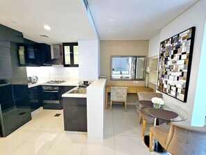 A modern kitchen with a central island, a dining area with a glass table, and a decorative wall piece. - Sunrise Homes - Chic Studio close to Dubai Mall with Canal Views (Business Bay)
