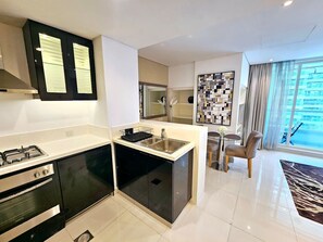 A modern kitchen with black cabinets, a gas stove, and a sink. There is a dining area with a chair and a rug.