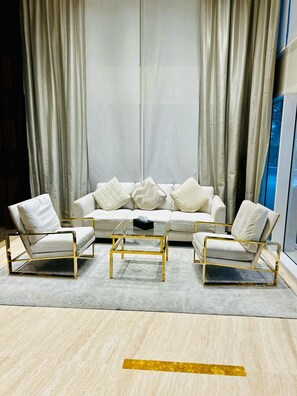 Una sala moderna con un sofá blanco, dos sillones y una mesa de centro de vidrio.