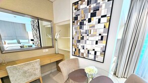 A modern hotel room with a large mirror, a glass table with two chairs, and a decorative wall piece.