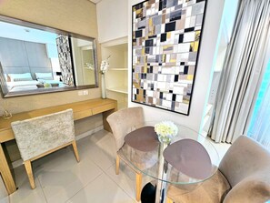 A modern hotel room with a large mirror, a glass table with two chairs, and a decorative wall piece.