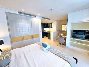 A modern hotel room with a large bed, a desk, a TV, and a kitchenette. - Sunrise Homes - Chic Studio close to Dubai Mall with Canal Views (Business Bay)