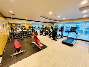 A gym with various exercise equipment, a treadmill, and a bench. - Sunrise Homes - Chic Studio close to Dubai Mall with Canal Views (Business Bay)