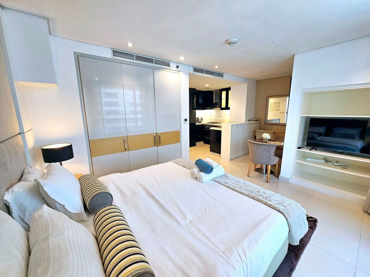 A modern hotel room with a large bed, a desk, a chair, a TV, and a wardrobe.