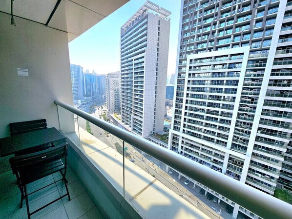 Un balcón con barandilla metálica, un banco negro y vistas a edificios altos.