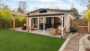 Un patio cubierto con mobiliario exterior, una parrilla para barbacoa y un césped bien cuidado.