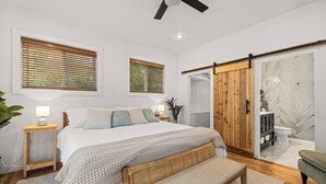 Un dormitorio moderno con cama, mesitas de noche, un banco y una puerta corredera que da al baño.