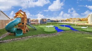 Een speelterrein met een glijbaan en klimconstructie, een putting green en een klein waterpartij.