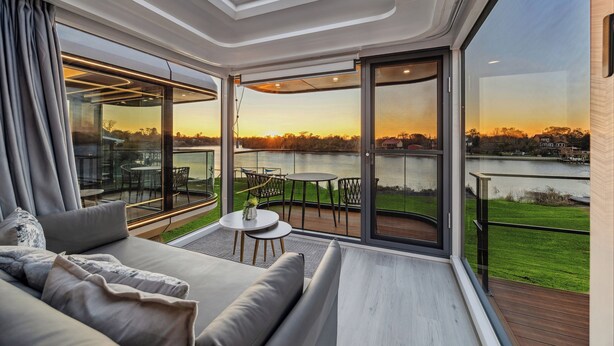 Een modern interieur met een bank, een tafeltje en uitzicht op een meer bij zonsondergang.