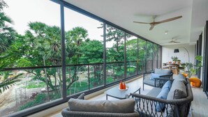A modern room with large windows, wicker furniture, and a view of greenery outside. - Beachside Residences by NLA (Choeng Thale)