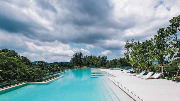 A swimming pool with a clear blue water, surrounded by lounge chairs and greenery. - Beachside Residences by NLA (Choeng Thale)