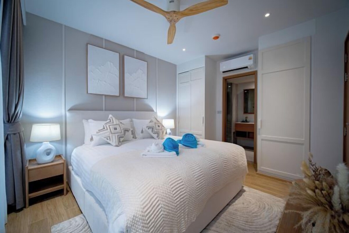 A hotel room with a large bed, bedside tables, a ceiling fan, and a door leading to a bathroom.