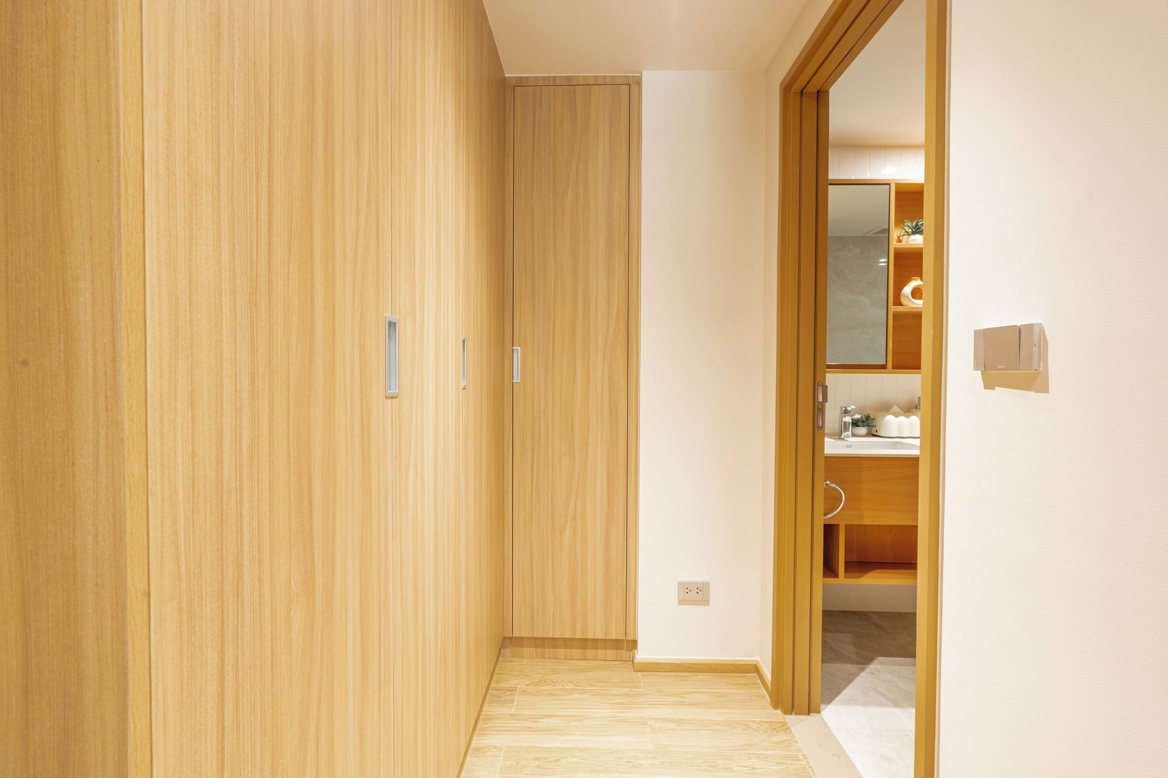 Un pasillo con paredes y piso de madera que conduce a un baño con lavamanos y espejo.