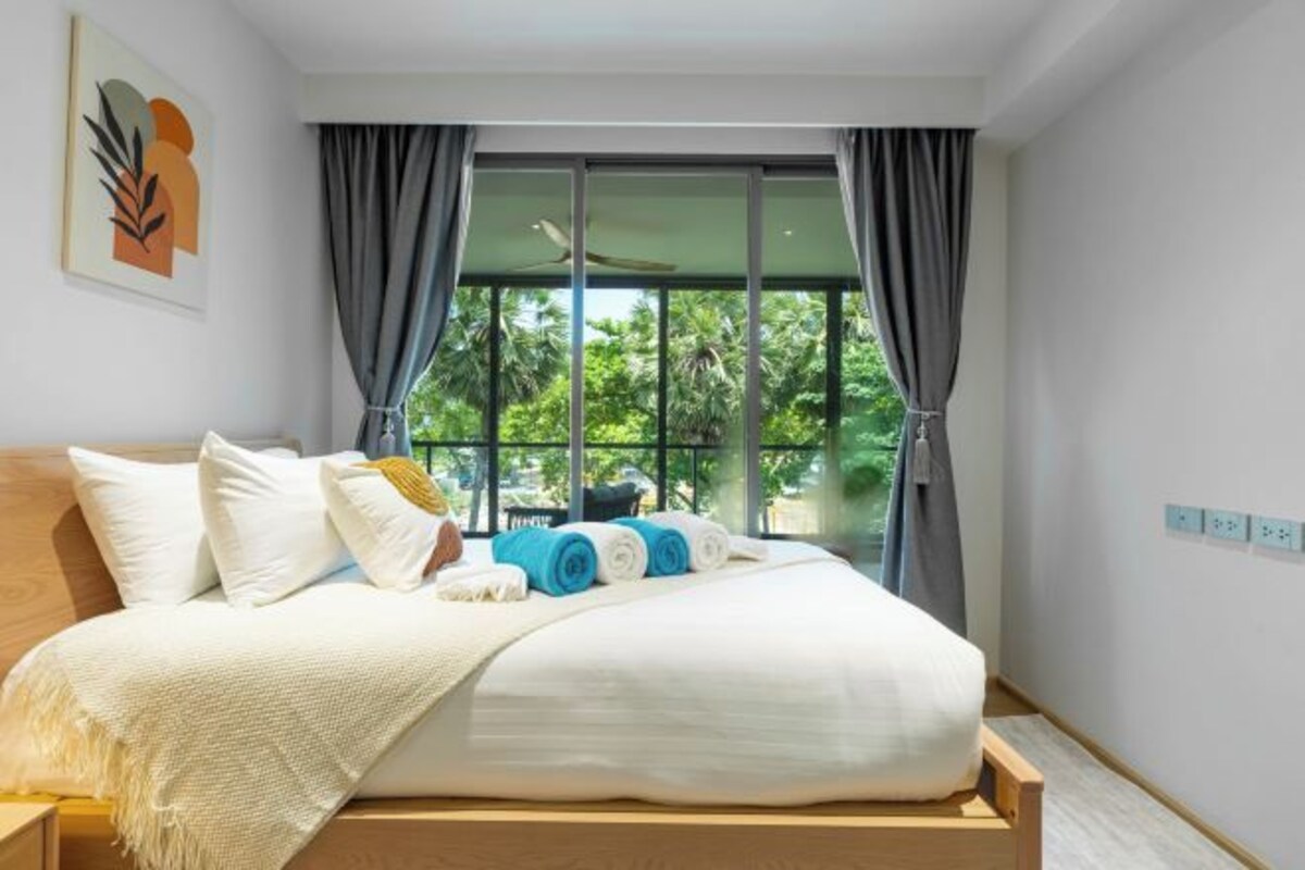 A modern bedroom with a large bed, a view of greenery outside, and a ceiling fan.