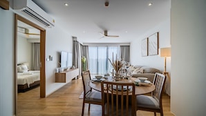 A modern living room with a dining area, wooden flooring, and a ceiling fan. - Beachside Residences by NLA (Choeng Thale)