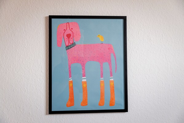 Uma obra de arte emoldurada de um cão rosa com botas laranja e um pássaro amarelo em suas costas.