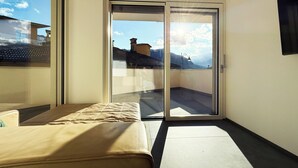 A balcony with a sliding glass door, a bed, and a view of buildings and mountains. - Apartment in the center of Levico with 3 bedrooms, 2 bathrooms, terrace,garage and elevator (Levico Terme)