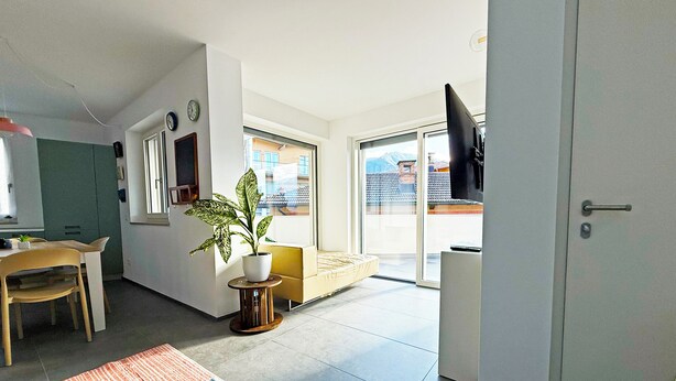 A modern living room with a dining area, a potted plant, a sofa, and a TV mounted on the wall. - Apartment in the center of Levico with 3 bedrooms, 2 bathrooms, terrace,garage and elevator (Levico Terme)