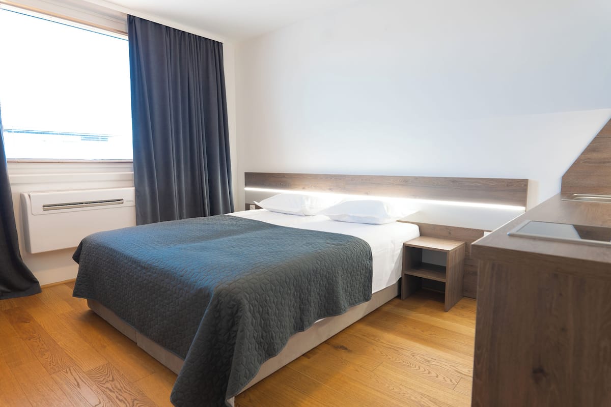 A modern hotel room with a bed, bedside table, and a built-in desk with a chair.