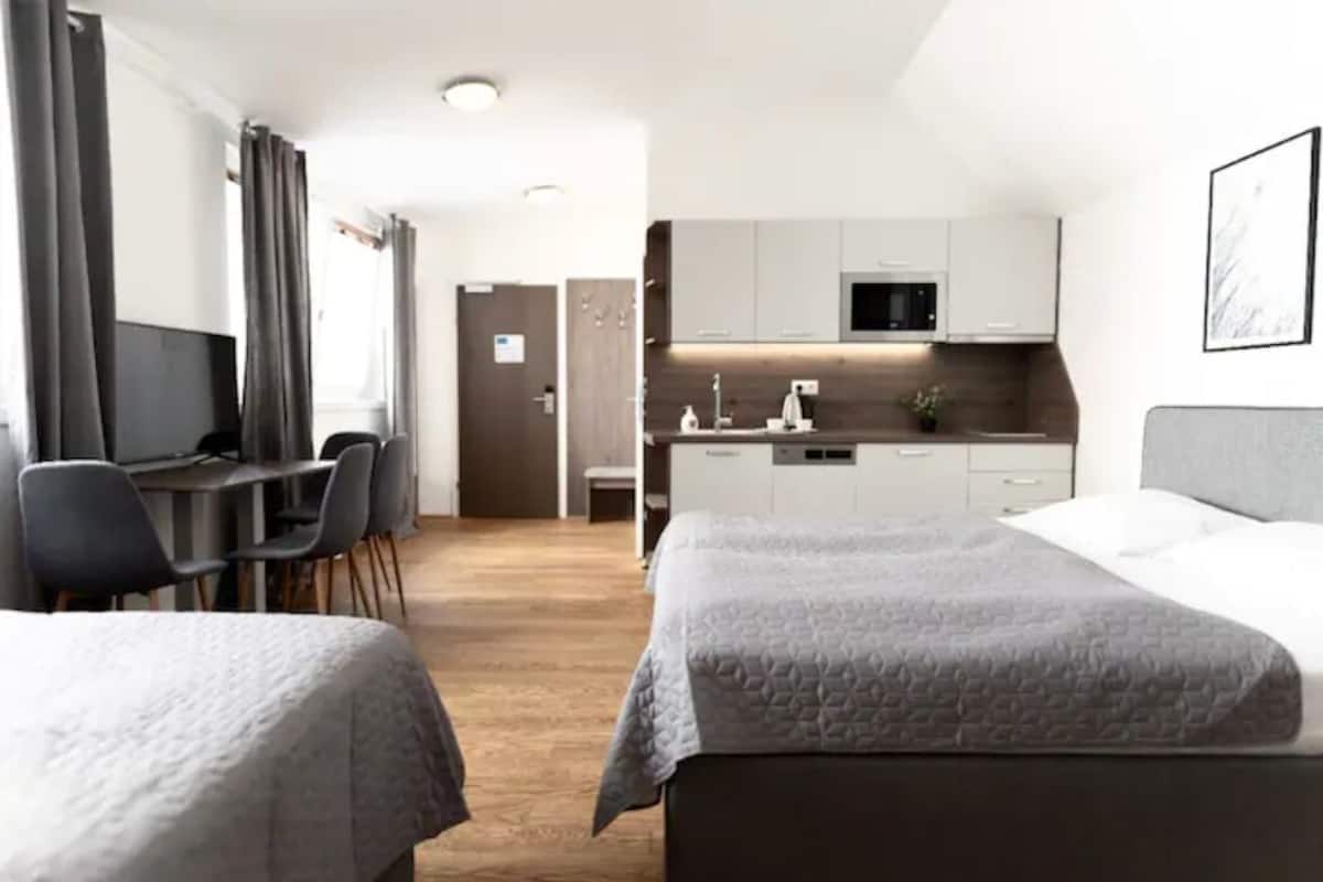 A hotel room with two beds, a desk, and a kitchenette.