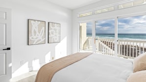 Un dormitorio con una cama grande, vista a la playa y dos obras de arte abstractas en la pared.