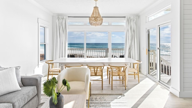 Un luminoso espacio habitable tipo loft con un ventanal que da al océano, una mesa de comedor con sillas y un sofá.