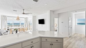 Una cocina moderna con una isla grande, armarios blancos y un televisor de pantalla plana montado en la pared.