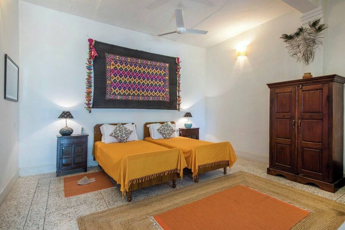 Une chambre avec deux lits, une armoire en bois, une décoration murale et un ventilateur de plafond.