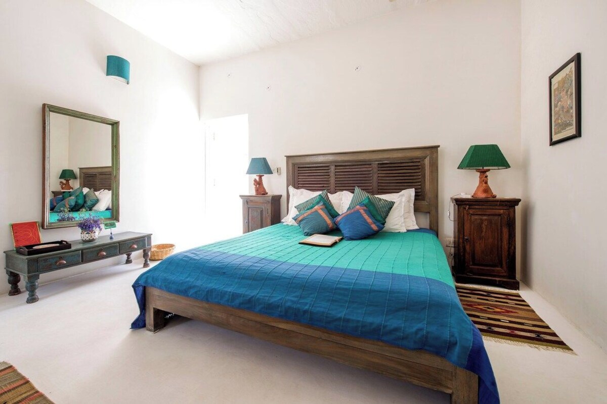 Un dormitorio con cama, mesitas de noche, cómoda, espejo y una puerta.